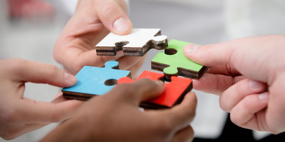 Mehrere Menschen halten Puzzleteile in einem Kreis zusammen - Bildausschnitt auf die Hände