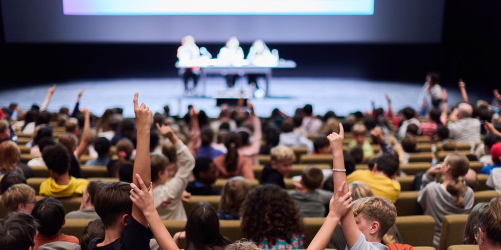 Viele Kinder im Saal bei einer Vorlesung. EInige melden sich