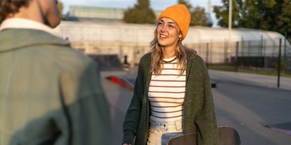 Junge Frau steht in Skatepark mit einem Skateboard und unterhält sich
