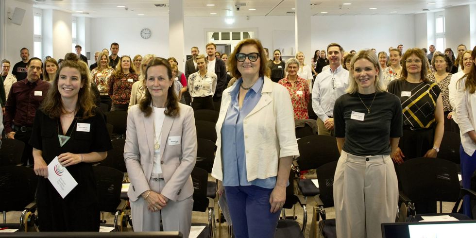 Pressefoto der Bündnistagung mit den Akteurinnen des Projekts "Fachkräftesicherung in der Pflege" und den Teilnehmenden. Vorne stehen v.l.n.r.: Katrin Mauch von ArbeitGestalten, XX, Senatorin Dr. Ina Czyborra, Leonie Teubel von der Senatsverwaltung für Wissenschaft, Gesundheit und Pflege und Sandra Tausch von ArbeitGestalten. Sie alle stehen in einem hellen Raum und blicken lächelnd in die Kamera.