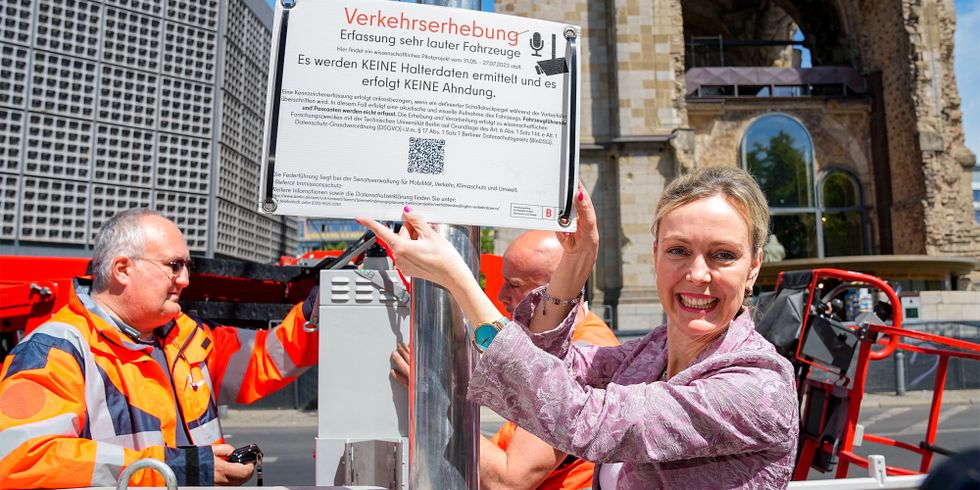 Senatorin Manja Schreiner präsentiert Lärmblitzer und zeigt Hinweisschild zum Verkehrsversuch.