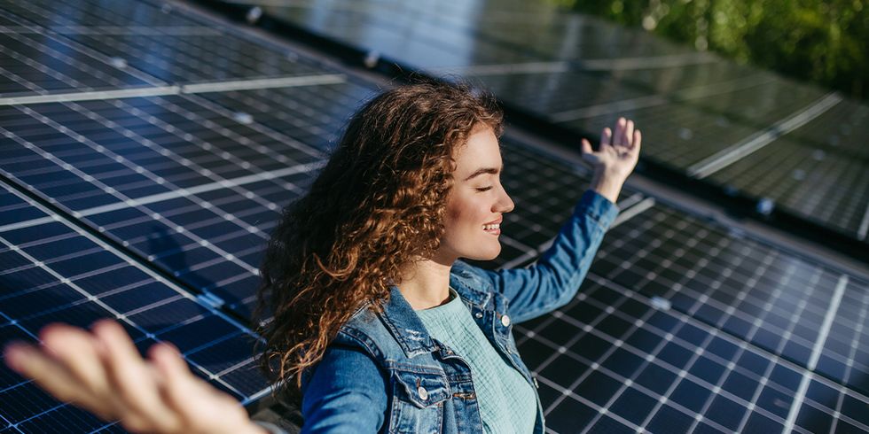 Frau lächelnd in Yogaposition auf dem Dach, Solaranlage im Hintergrund