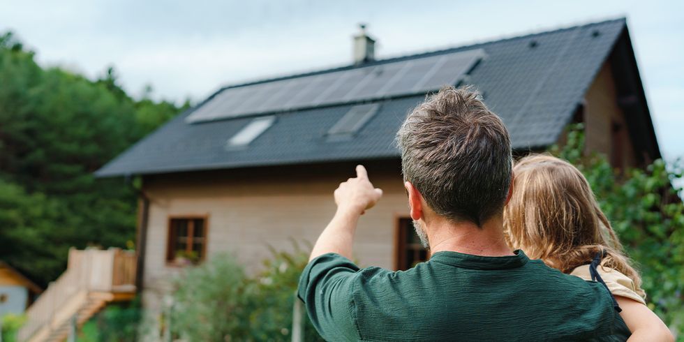 Mann mit Kind auf dem Arm vor einem Einfamilienhaus mit Solaranlage auf dem Dach