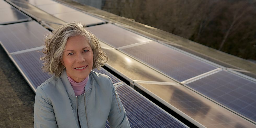 Einer lächelnde Frau mit kurzen Haaren vor Solarpanelen auf einem Dach.