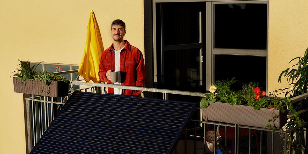 Lächelnder Mann auf Balkon in der Sonne. Am Balkon ist ein Solarmodul angebracht.