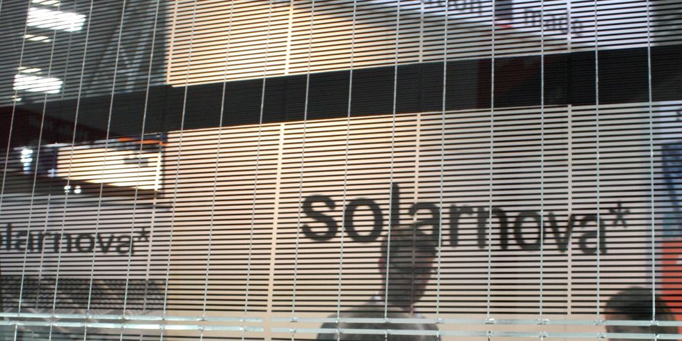 Bild eines semitransparenten Solarmoduls mit Siliziumlamellen durch das hindurch man Menschen auf einer Messe sieht.