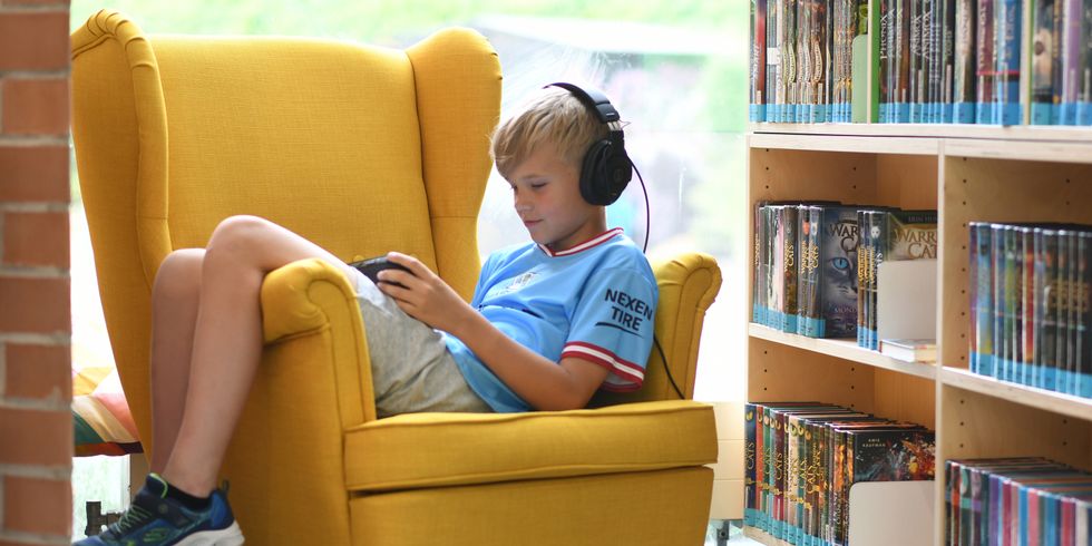 Junge in einem gemütlichen Sessel in der Bibliothek. Er spielt ein Videospiel.