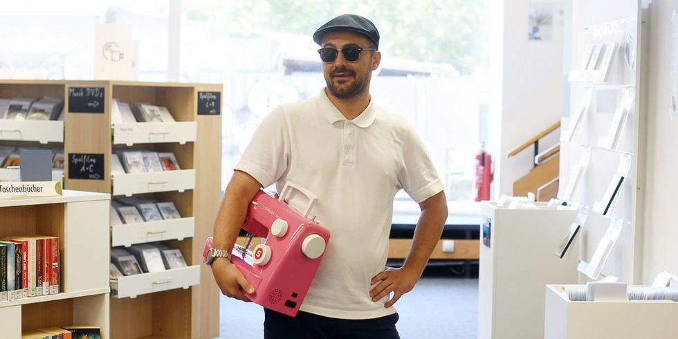 Ein Mann hält eine pinke Nähmaschine in einer Bibliothek