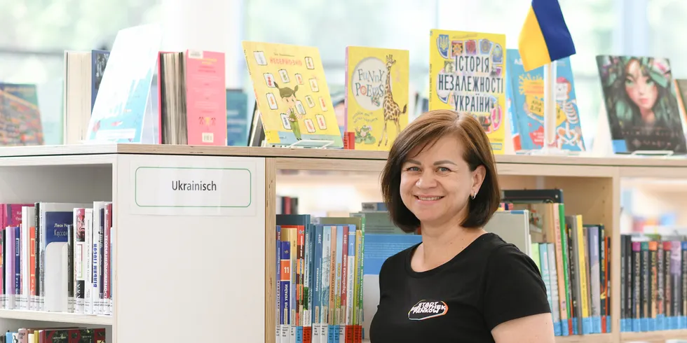 Bibliothekarin steht vor einem Regal mit ukrainischsprachigen Bücher und einer Ukrainefahne