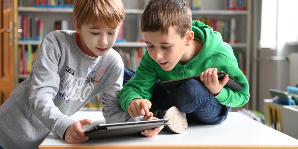 Zwei Kinder in Grundschulalter arbeiten mit Tablets in einer Bibliothek.