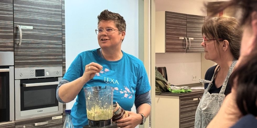 Kursleiterin Alexa Adam erklärt etwas. Sie steht hinter einem gefülltem Mixer und schau nach links.