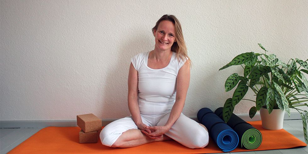 Kursleiterin Tanja Gentsch sitzend auf einer organefarbenen Yogamatte