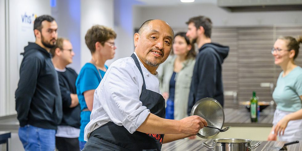 Victor Mendivil am Herd in der Lehrküche, im Hintergrund Kursteilnehmer:innen