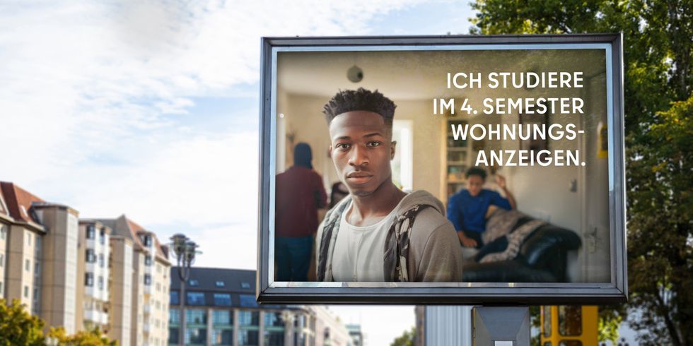 Auf einer Werbetafel in Berlin ist ein junger Mann abgebildet, der direkt in die Kamera blickt. Hinter ihm sind weitere Personen in einem Raum. Der Text auf der Tafel lautet: “ICH STUDIERE IM 4. SEMESTER WOHNUNGSANZEIGEN.” Im Hintergrund sieht man städtische Gebäude und Straßen.