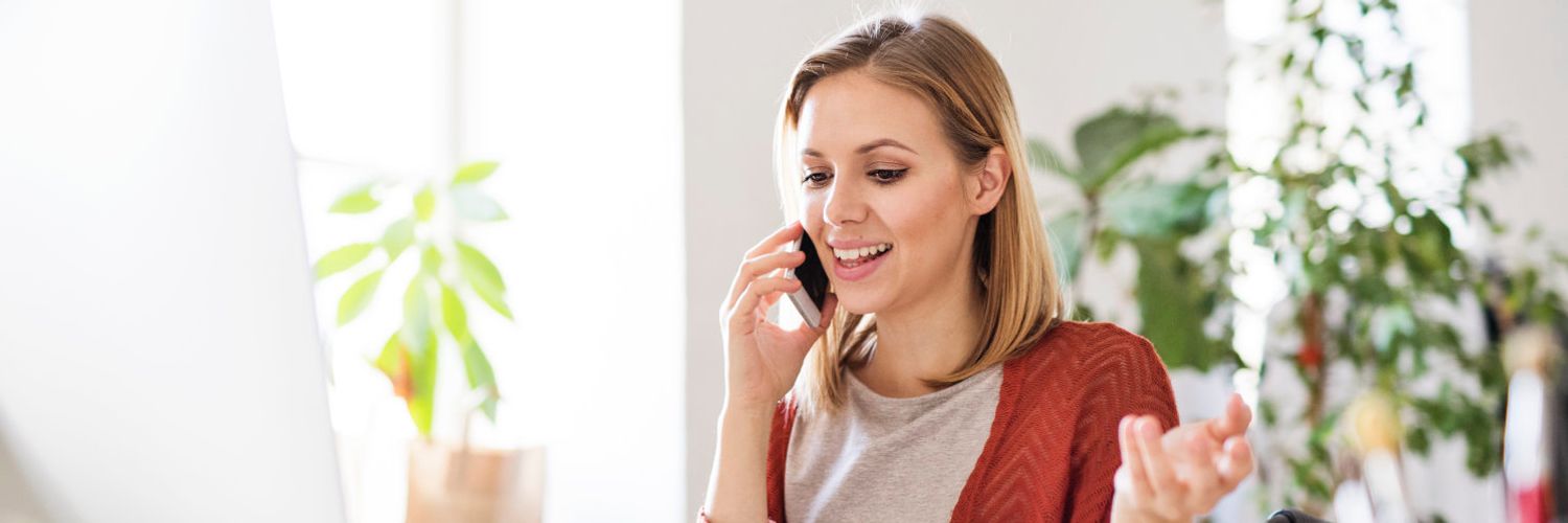 Eine Frau sitzt an einem modernen Arbeitsplatz und telefoniert mit ihrem Mobiltelefon