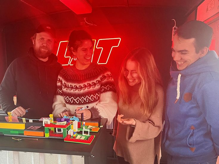 Vier Jugendliche vor roter Leuchtschrift, auf einem Tisch Lego