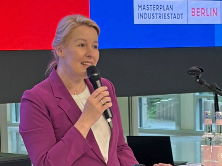 Franziska Giffey spricht in ein Mikrofon, sie trägt eine rosa Jacke und dunkelblaue Hose, auf dem Tisch vor ihr liegen weitere Mikrofone und ein Laptop, im Hintergrund ist eine Bildschirmprojektion mit dem Titel Masterplan Industriestadt Berlin zu sehen.