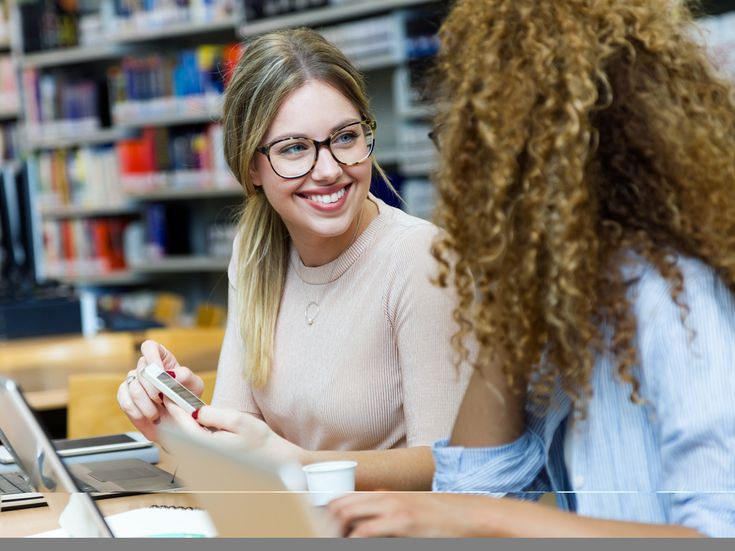 Zwei Studentinnen arbeiten an ihren Laptpops und sprechen dabei