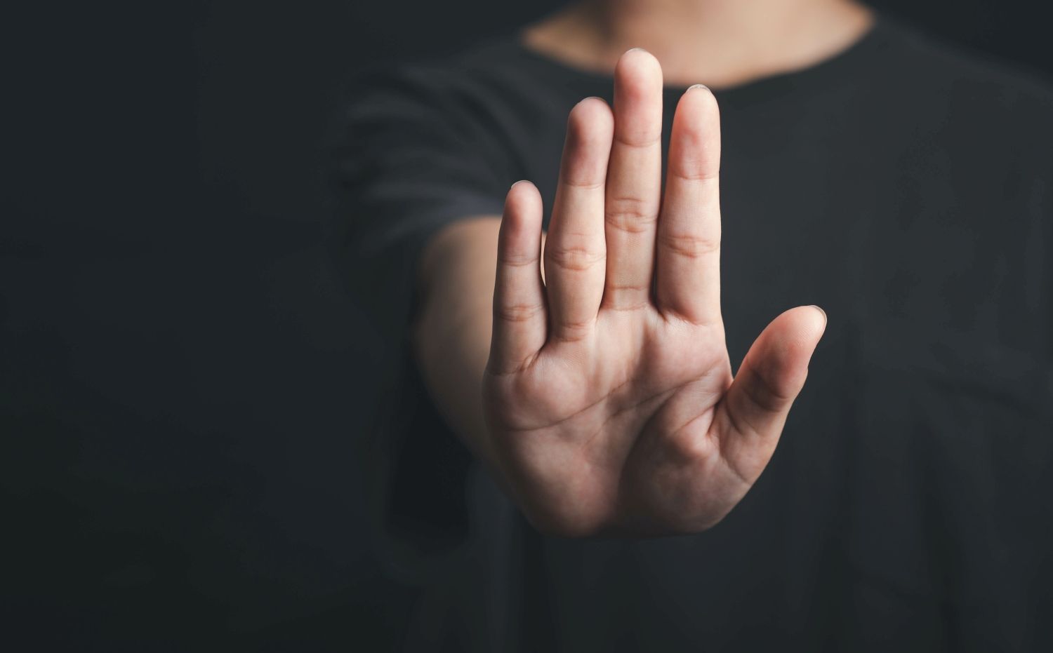 Nahaufnahme einer Hand, die nach vorne gehalten wird, als Signal für ‚Stopp‘ oder ‚Halt‘, vor unscharfem Hintergrund.