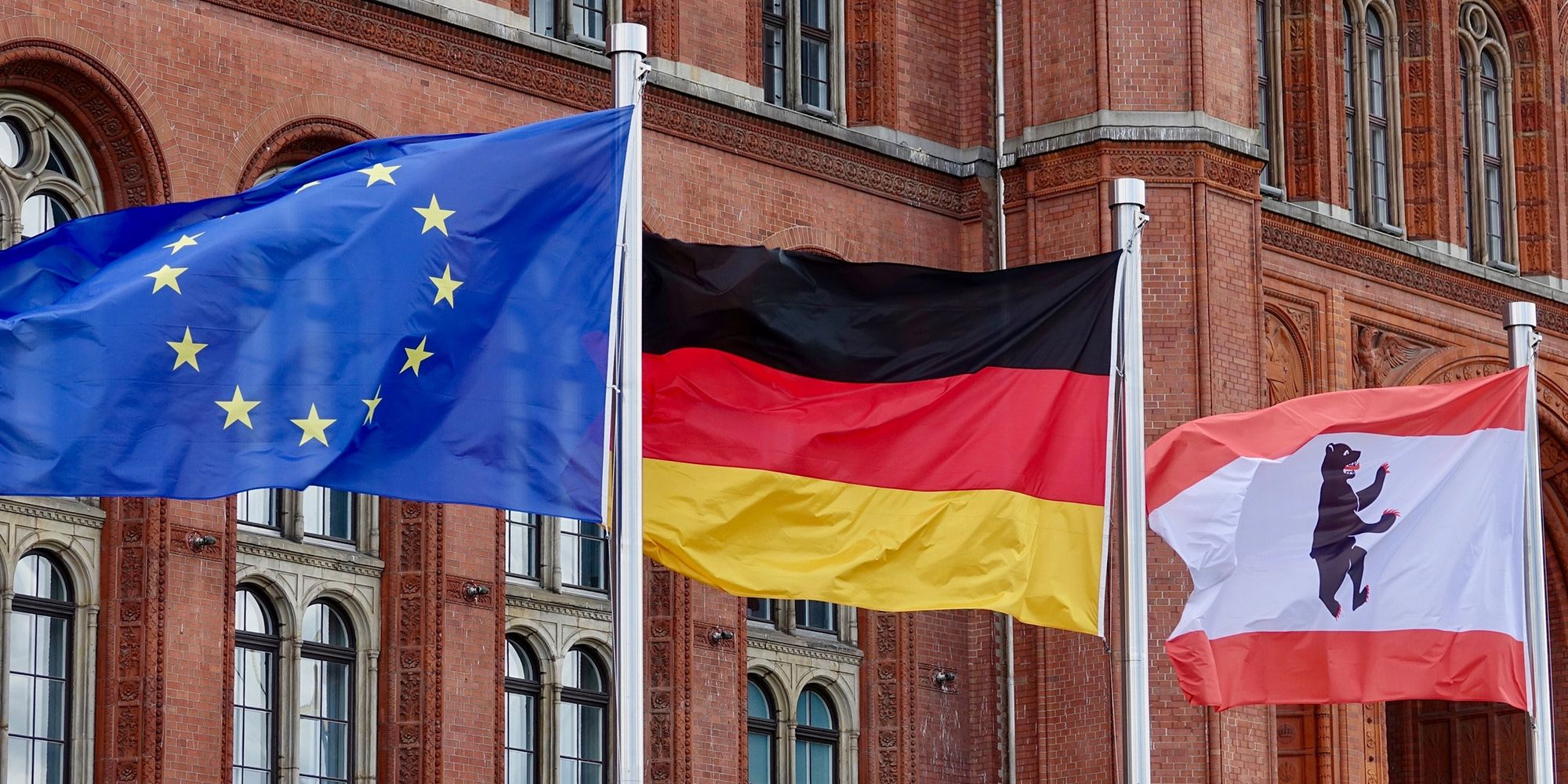 Drei wehende Flaggen vor dem Roten Rathaus, darunter die Europaflagge, die deutsche Flagge und die Berliner Landesflagge