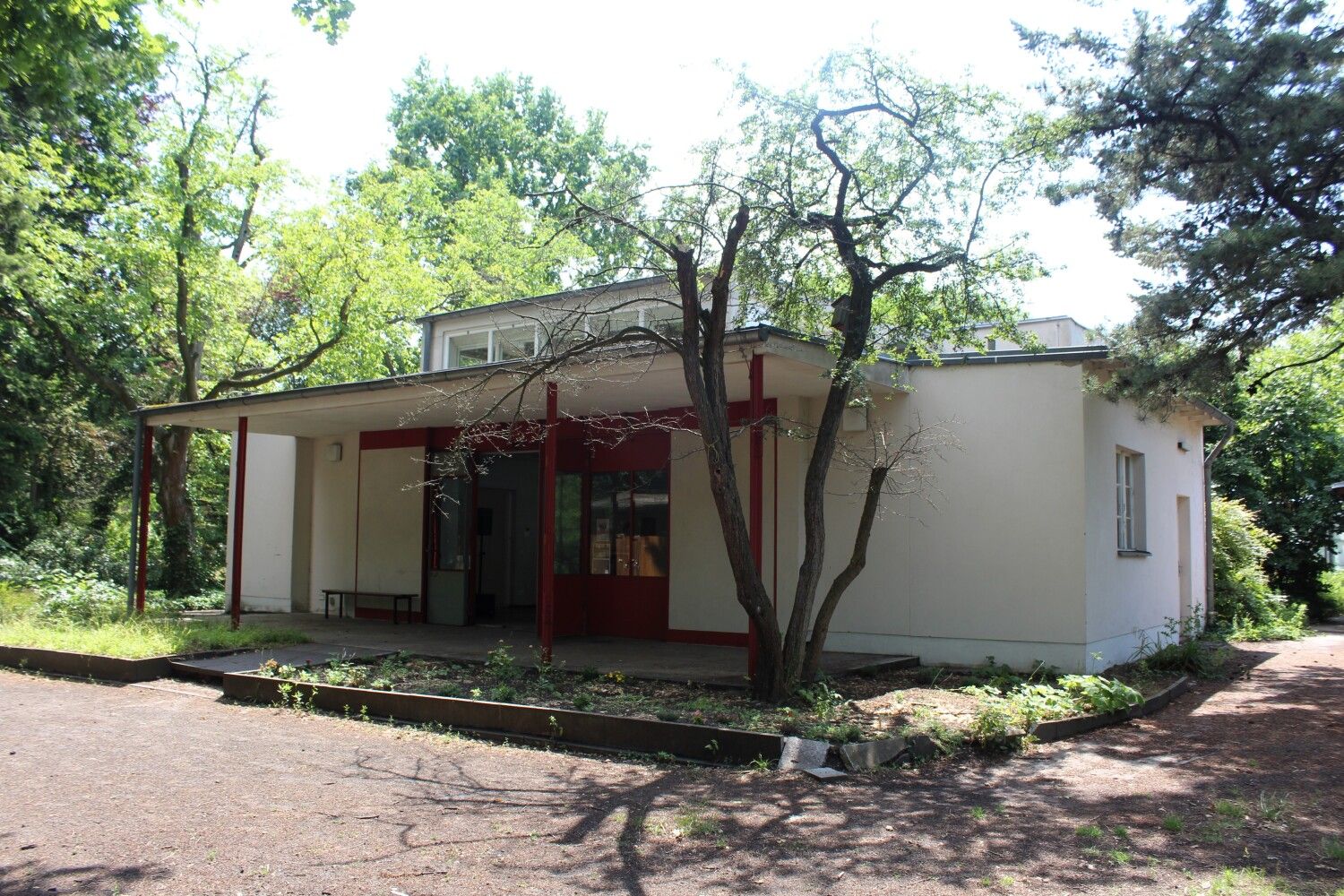 Versuchspavillion von Bruno Taut und Fritz Karsen: weißer Bungalow mit erhobenem Dach mit Fensterfront. Großer Eingangsbereich mit überdachter Terrasse