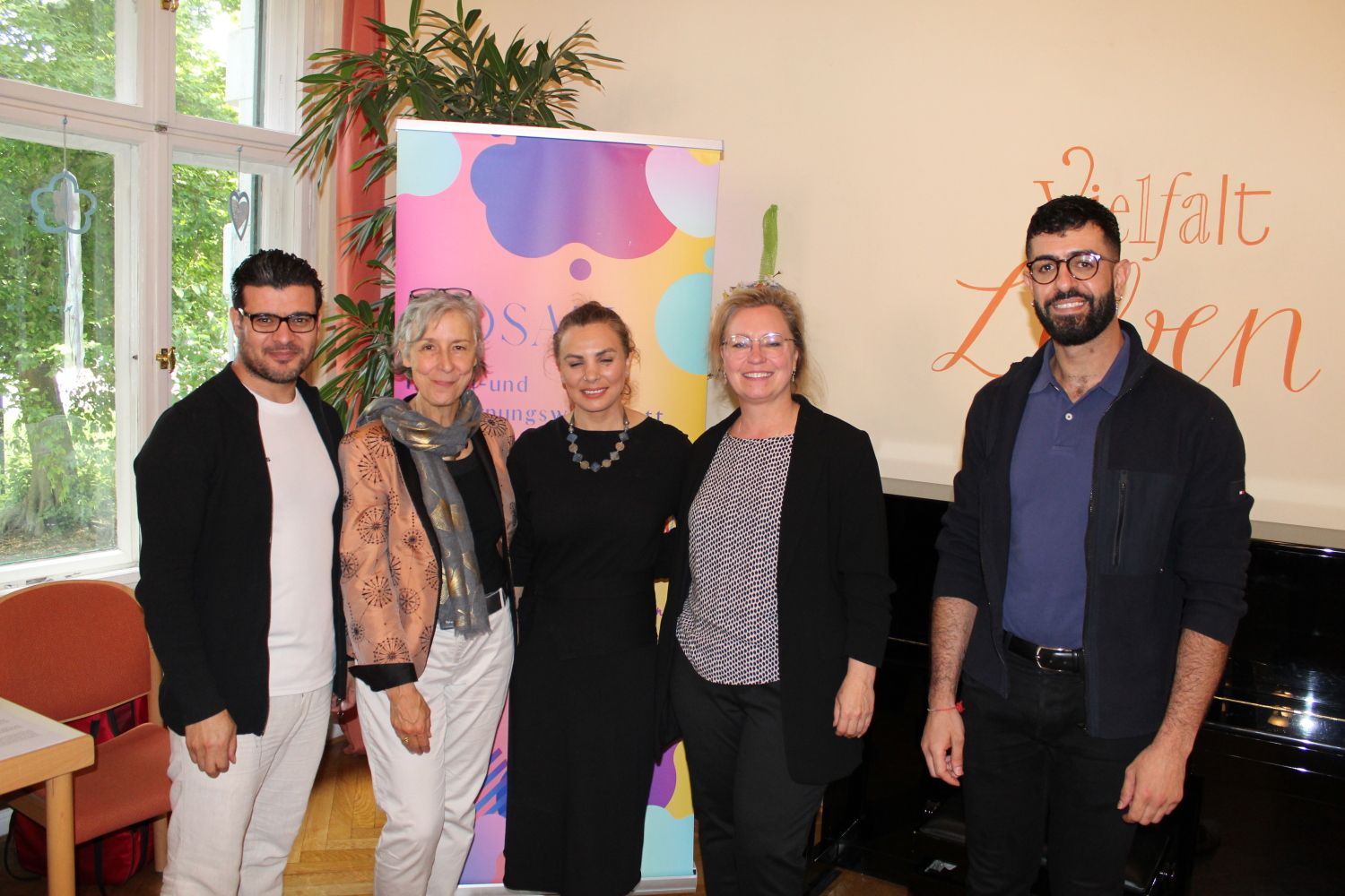 11. Juni 2024: Gruppenbild vor dem Mosaik-Logo mit (v.l.n.r.) mit Hareth Almukdad (Stadtteilarbeiter), Dr. Rita Zobel (Projektleiterin), Boshra Mustafa (Künstlerin) von der Mosaik Erzähl- und Begegnungswerkstatt mit der Freizeitstättenleiterin Stefanie Müller und dem Musiker Alaaddin Zaitounah