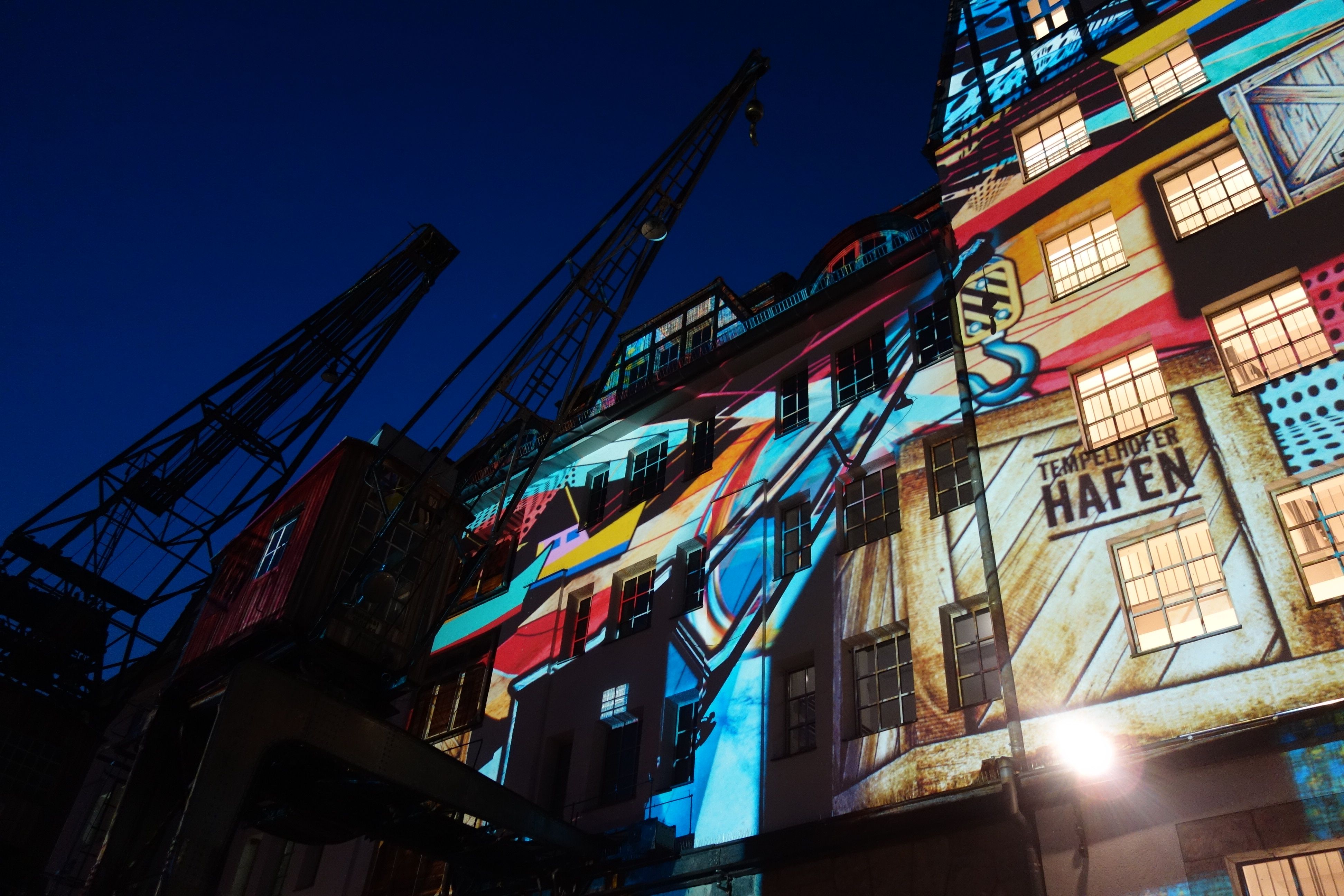 bunte Lichtprojektion auf auf ein Großes Gebäude mit Krähnen im Vordergrund