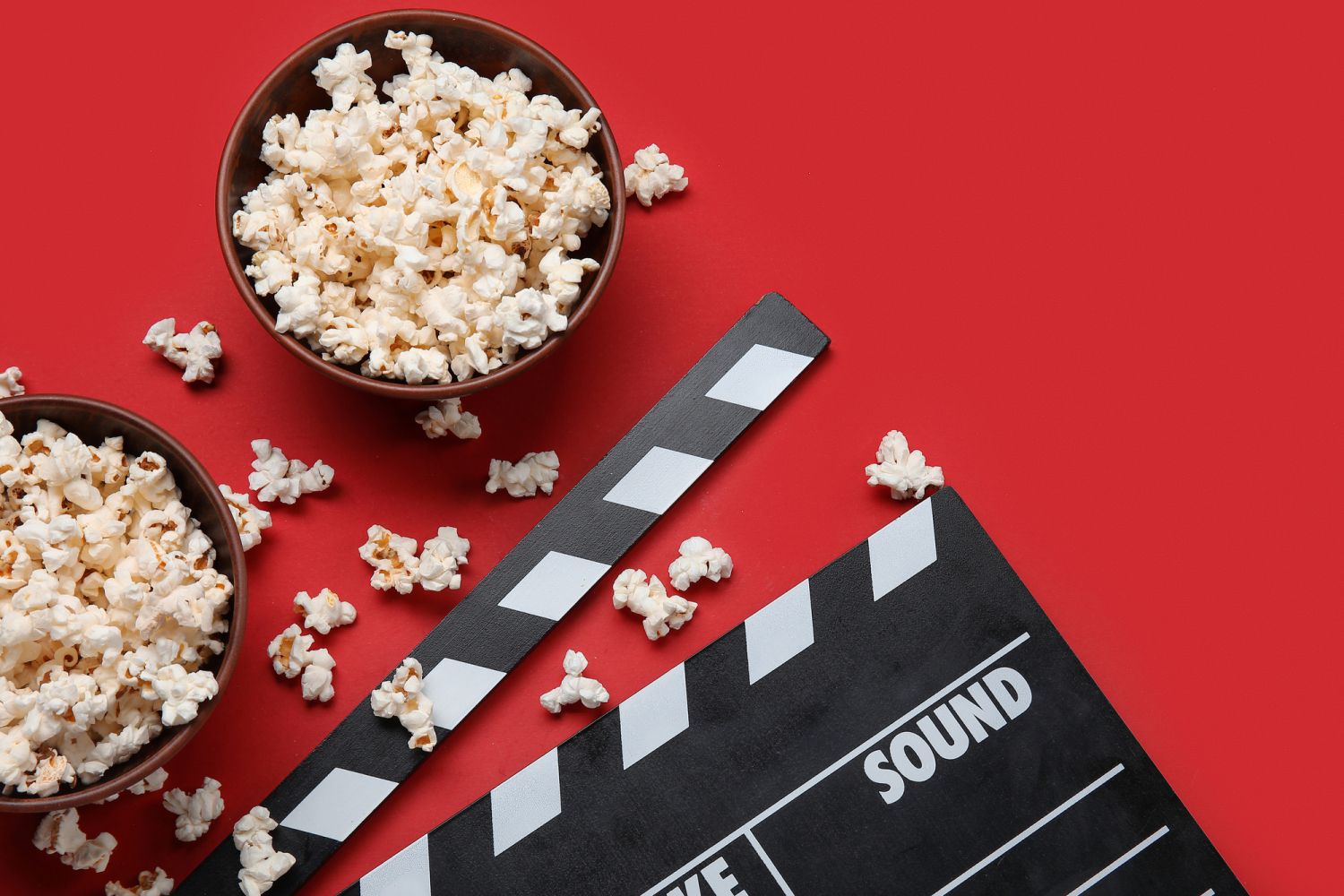 Schüsseln mit Popcorn und eine Filmklappe vor rotem Hintergrund
