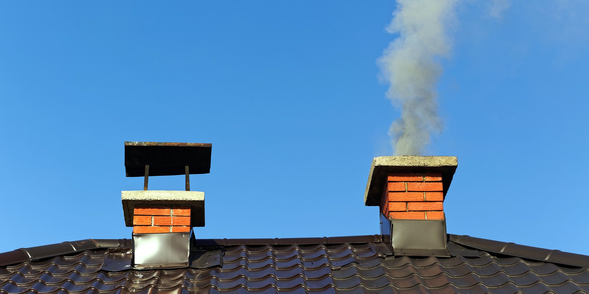 Rauch aus gemauertem Schornstein auf Dach gegen blauen Himmel