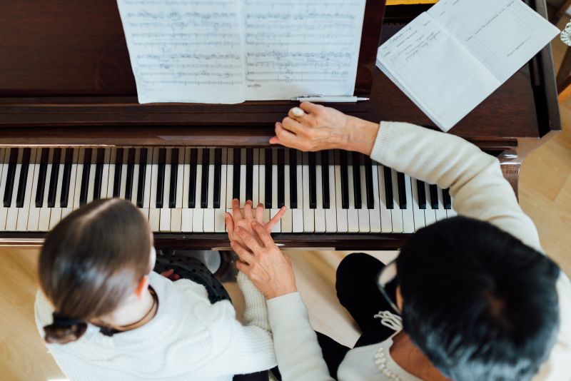 Musiklehrerin hilft Schülerin beim Klavier spielen