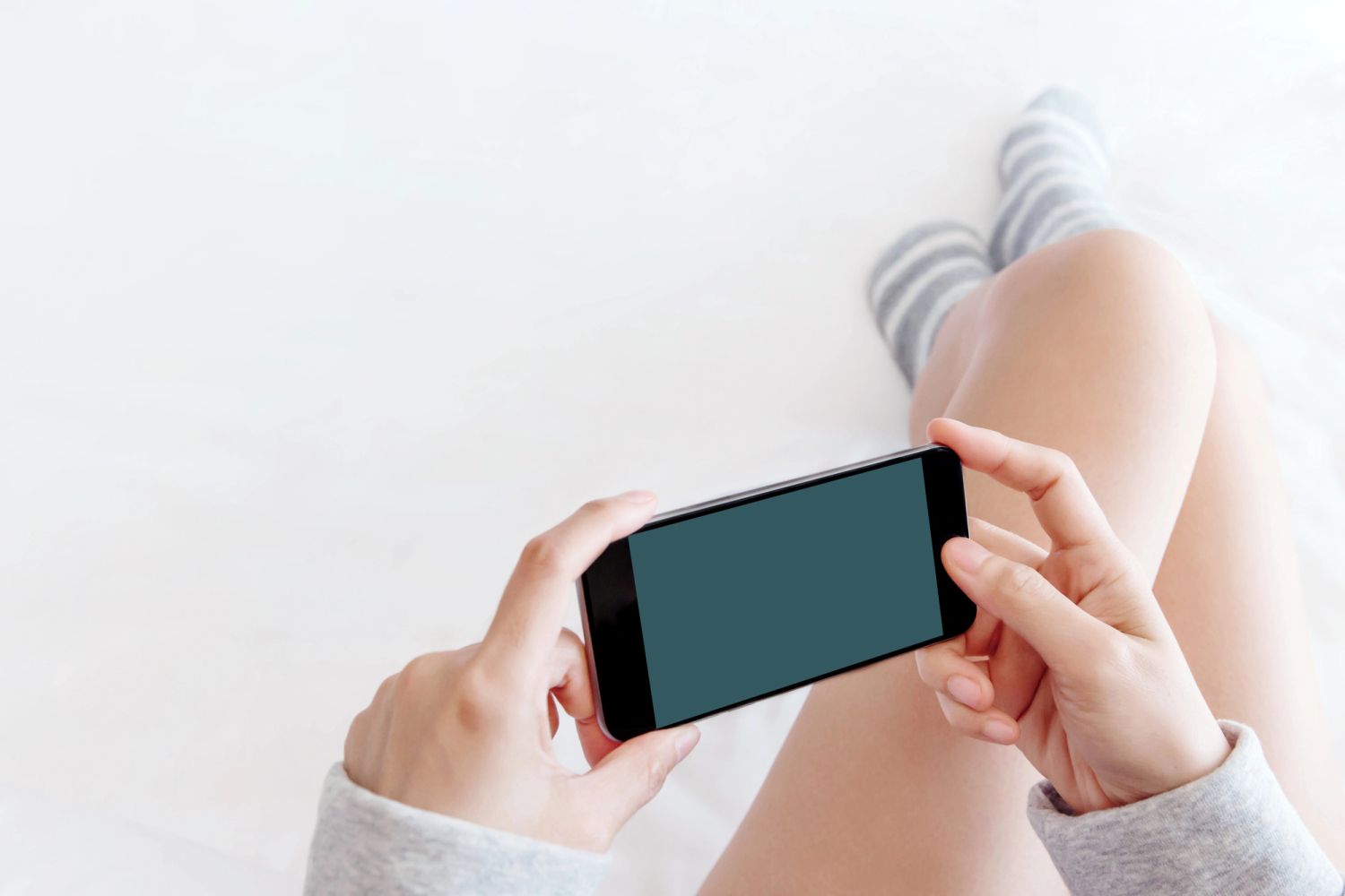 Eine Frau mit einen Handy in der Hand auf einem Bett