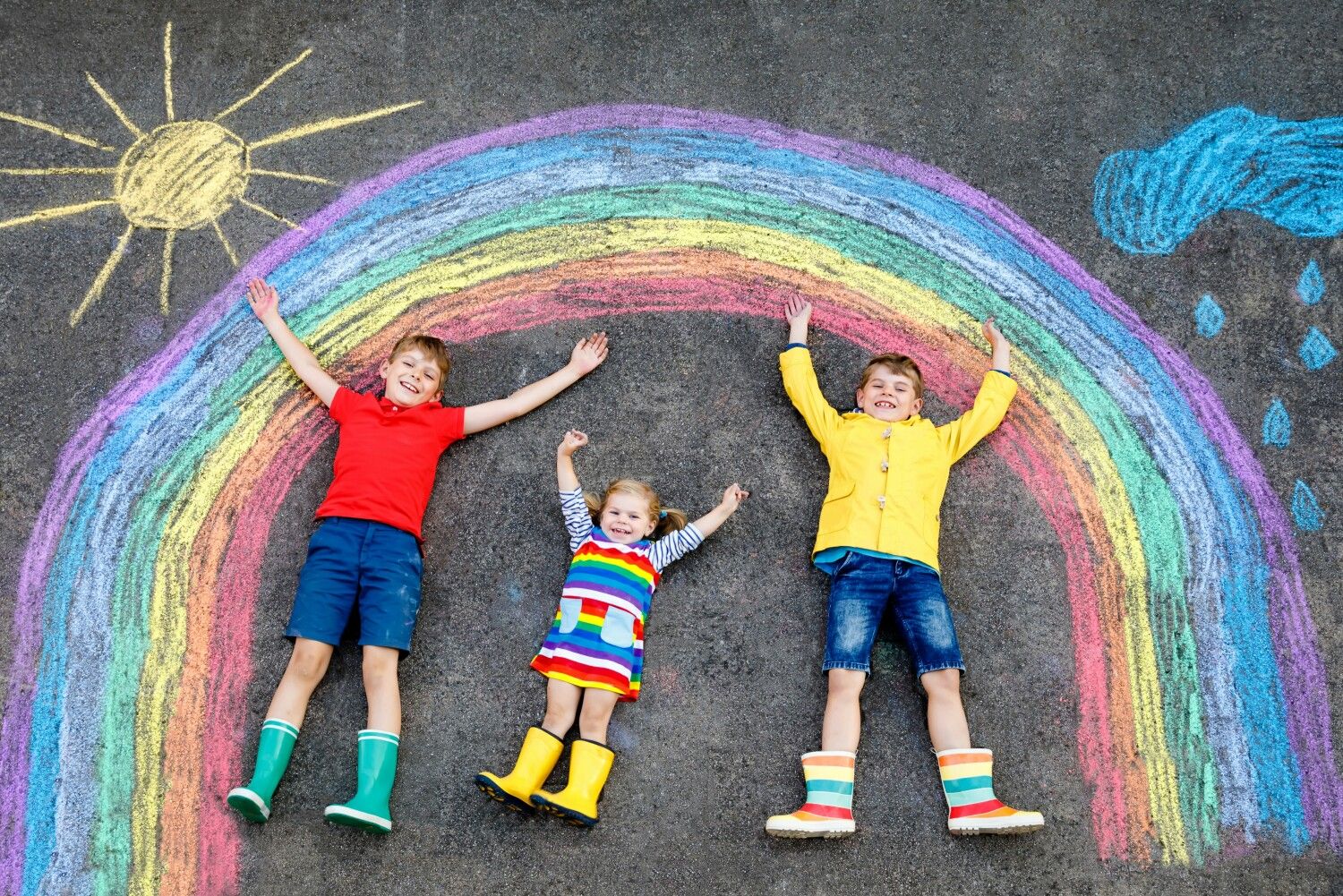 Kinder mit Malerei eines Regenbogens auf der Straße liegend