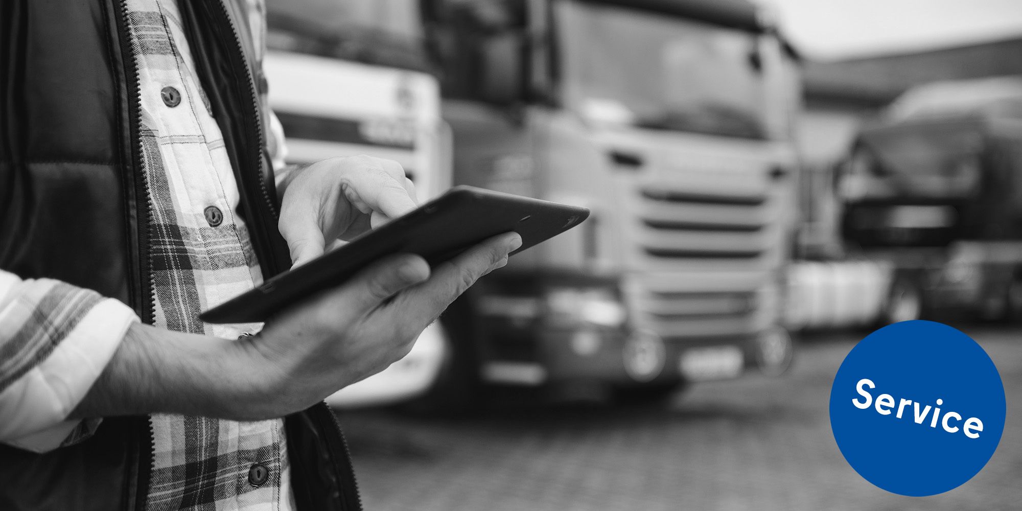 Mann mit digitalem Tablet, das den Flottenbetrieb und die Frachtlogistik steuert, steht in der Nähe einer Reihe von Transportfahrzeugen