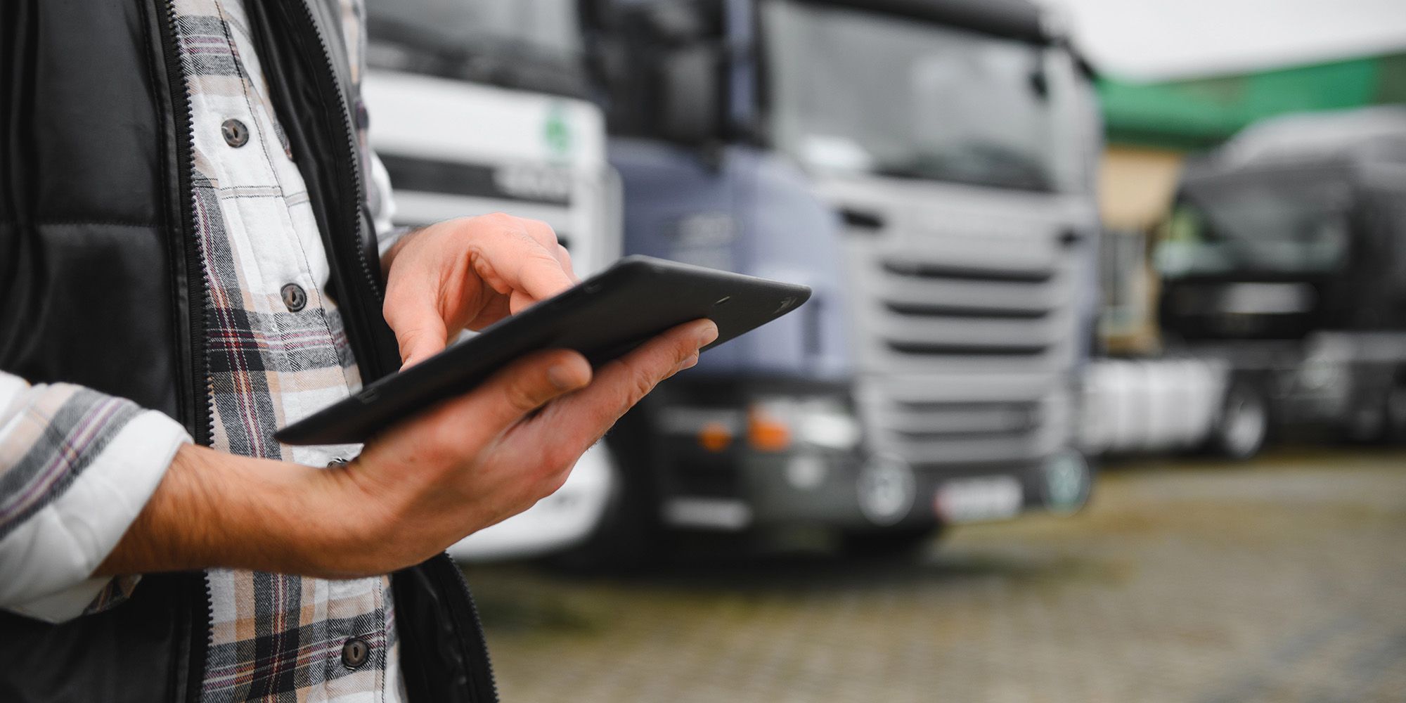 Mann mit digitalem Tablet, das den Flottenbetrieb und die Frachtlogistik steuert, steht in der Nähe einer Reihe von Transportfahrzeugen