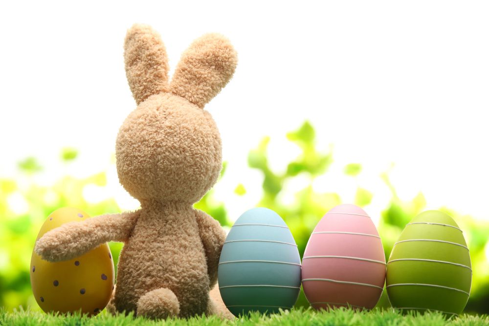 Plüschosterhase von hinten sitzt auf einer Wiese neben bunten Ostereiern
