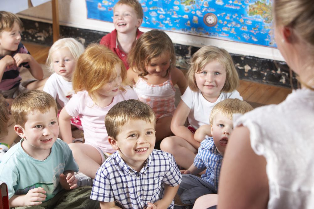 Kinder sitzen im Kindergarten auf dem Boden und hören Erzieherin zu