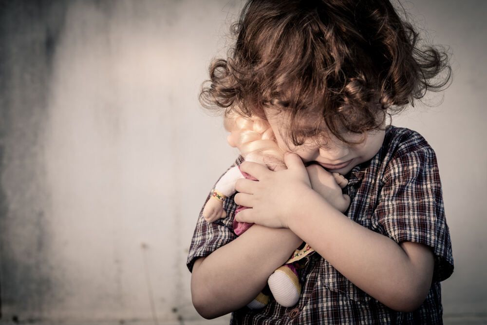 Trauriger kleiner Junge mit Puppe im Arm