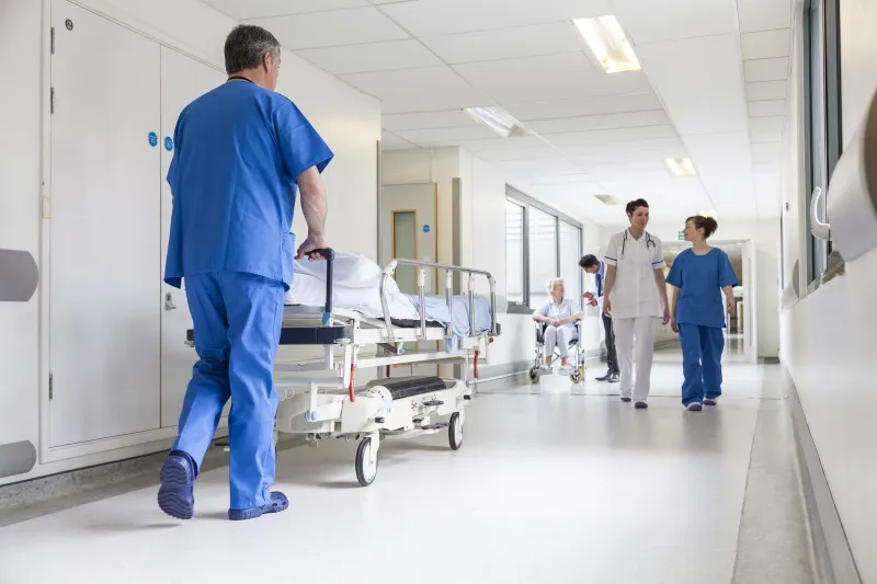 Mediziner schiebt Krankenbett durch Krankenhausflur