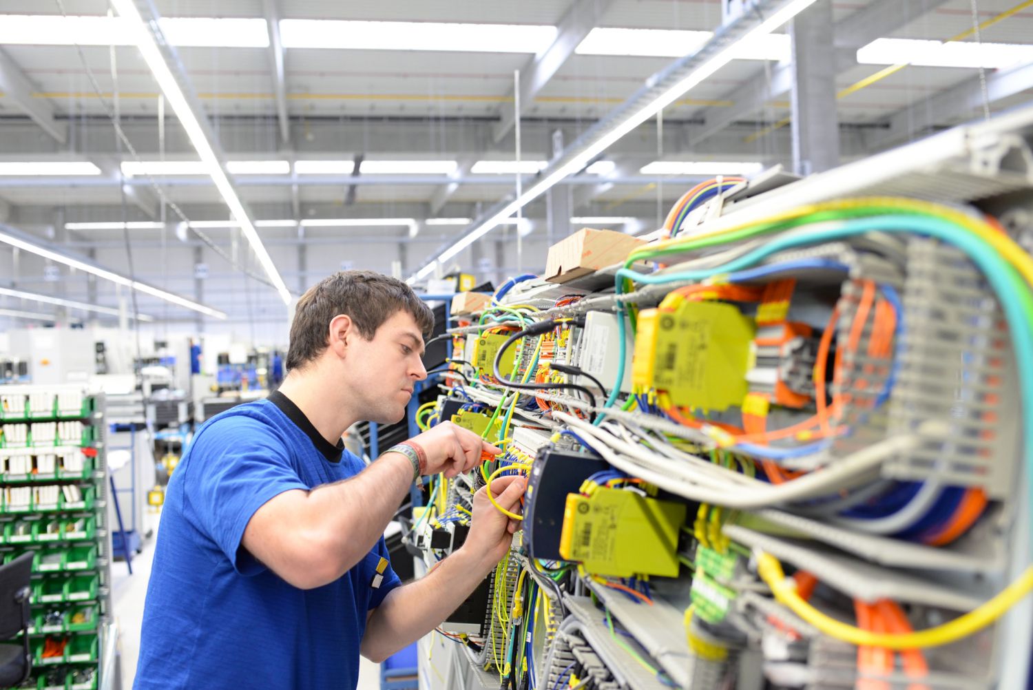 junger Mann verschraubt Komponenten und Kabel an einer Hutschiene