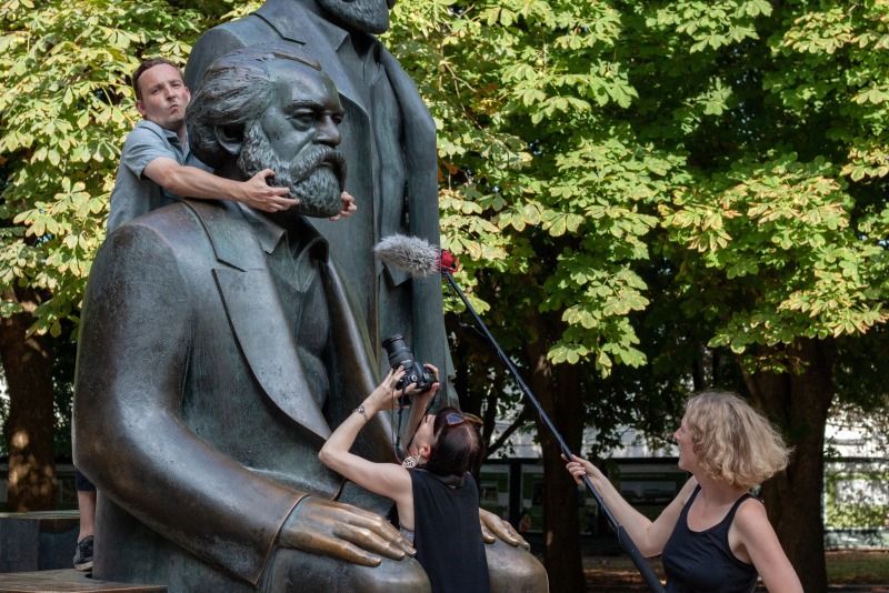 Ein Bronezedenkmal wird von 2 Personen interviewt