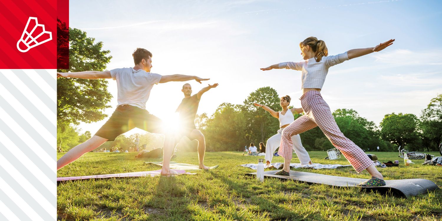 Menschen auf einer Wiese machen gemeinsam Yogaübungen bei Sonnenlicht.