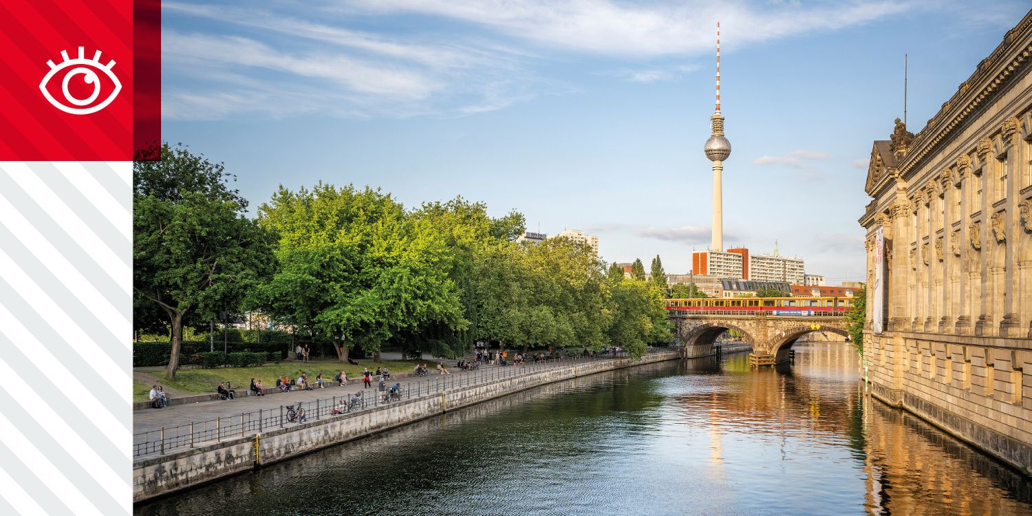 Spree mit Uferpromenade, Bäumen, Brücke und Fernsehturm im Hintergrund.