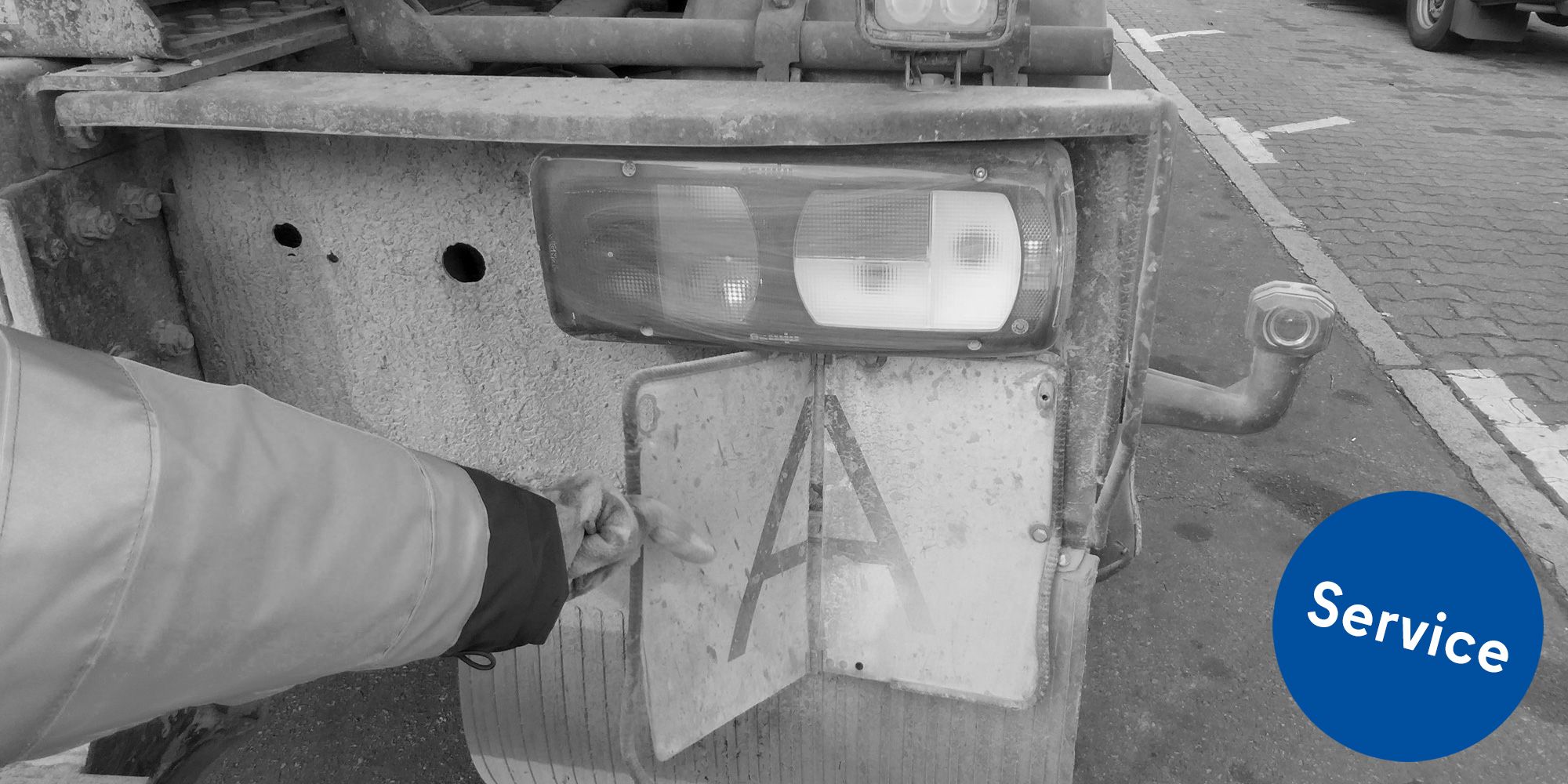 Ein Arm in Warnjacke hält ein Schild an das Heck eines Fahrzeugs, auf dem ein „A“ zu sehen ist. Dies zeigt an, dass in dem Fahrzeug Abfälle nach deutschem Recht transportiert werden.