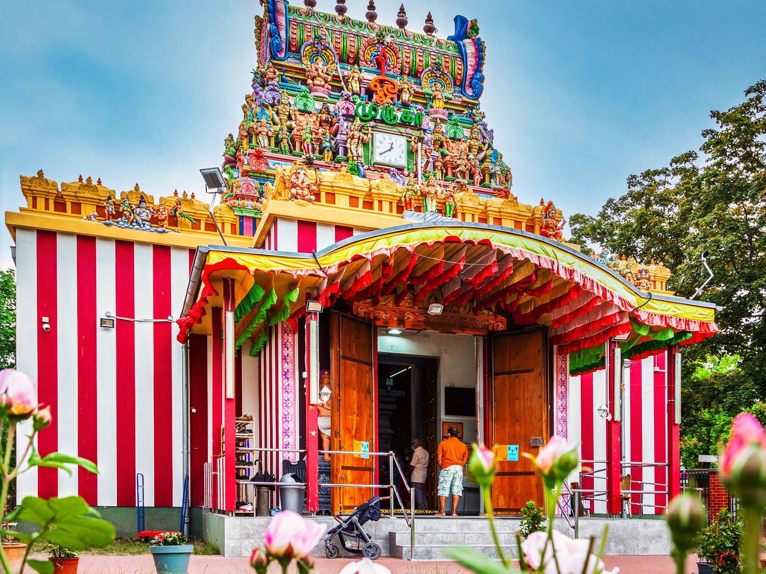 Ein Hindutempel. Der unterer Teil des Tempels ist rot-weiß gestreift gestrichen. Darüber eine Art Turm mit vielen hinduistischen Göttern. Die Götter sind sehr farbenfroh angemalt.