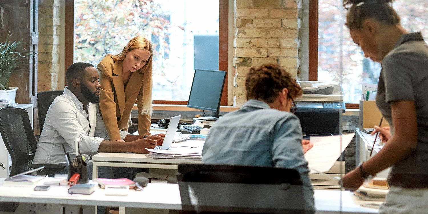 Zwei Frauen und zwei Männer im Büro jeweils in einem Gespräch an ihren Arbeitsplätzen