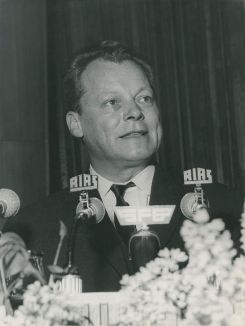 Enlarge photo: Close-up of a man behind several microphones, two of which say “Rias”.