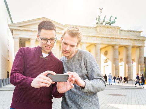 Zwei Männer schauen auf Smartphone, im Hintergrund Brandenburger Tor