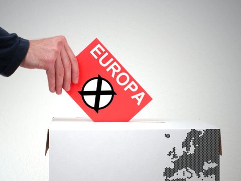 Eine Hand steckt einen roten Wahlumschlag mit der Aufschrift Europa in eine Wahlurne