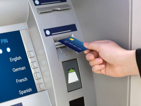 Jemand schiebt eine Bankkarte in einen Geldautomaten, auf dem Display kann zwischen verschiedenen Sprachen gewählt werden