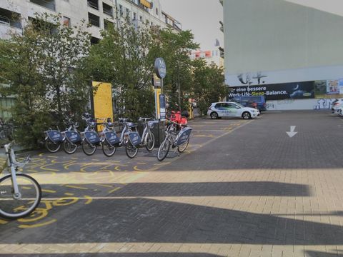 Jelbi-Station an der Schönhauser Allee, zu sehen sind Leihfahrräder, Leihroller, ein Informationsschild und ein Carsahringfahrzeug